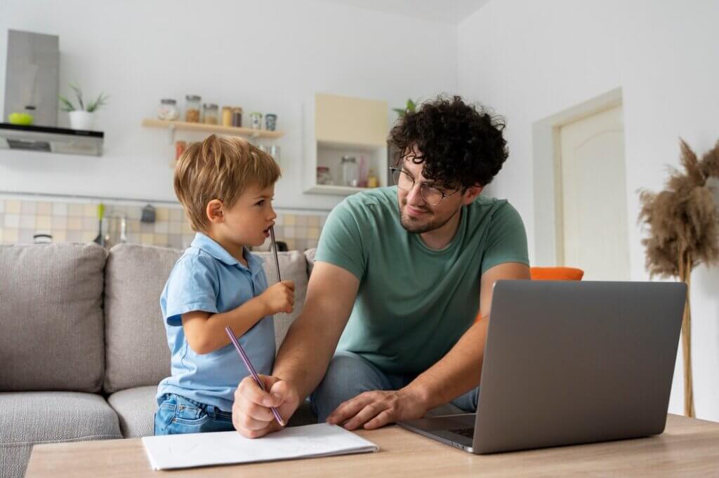 A parent and child engage in a learning activity at home, with a laptop and drawing materials on a table.