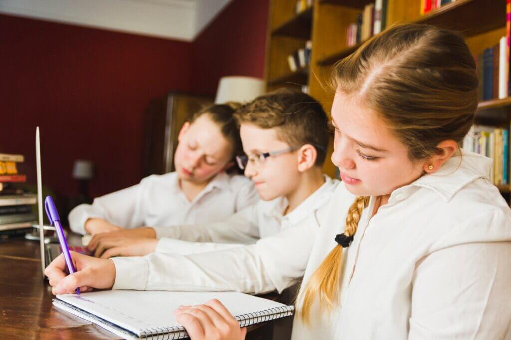 Three young students at a table, collaborating on a laptop in a secondary school setting.