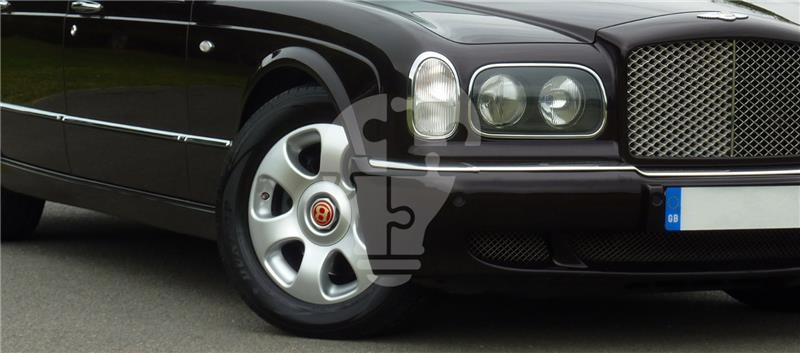 A close-up of the front wheel and grille of a dark-colored luxury car, showcasing its sleek design and distinctive emblem.