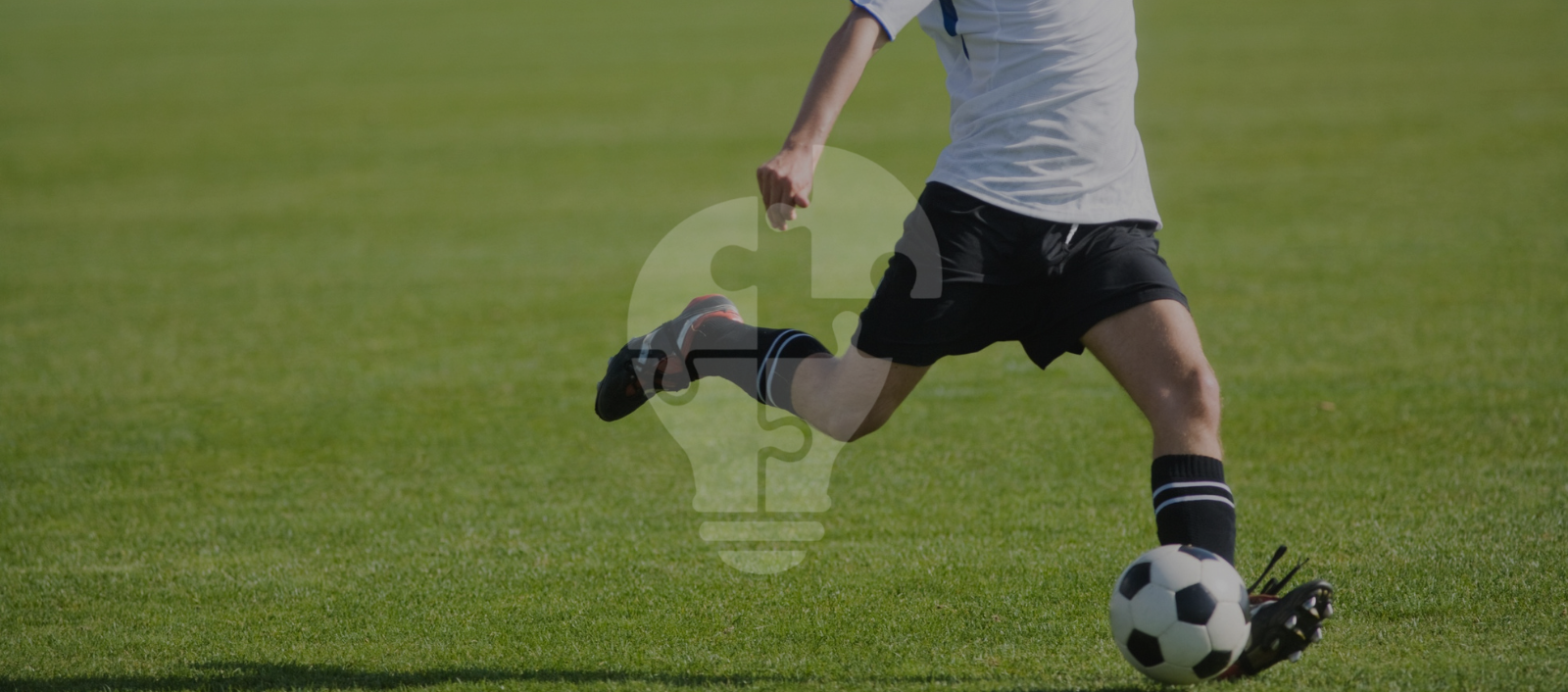 A soccer player in motion, striking a black and white ball on a lush green field, showcasing athleticism and focus.