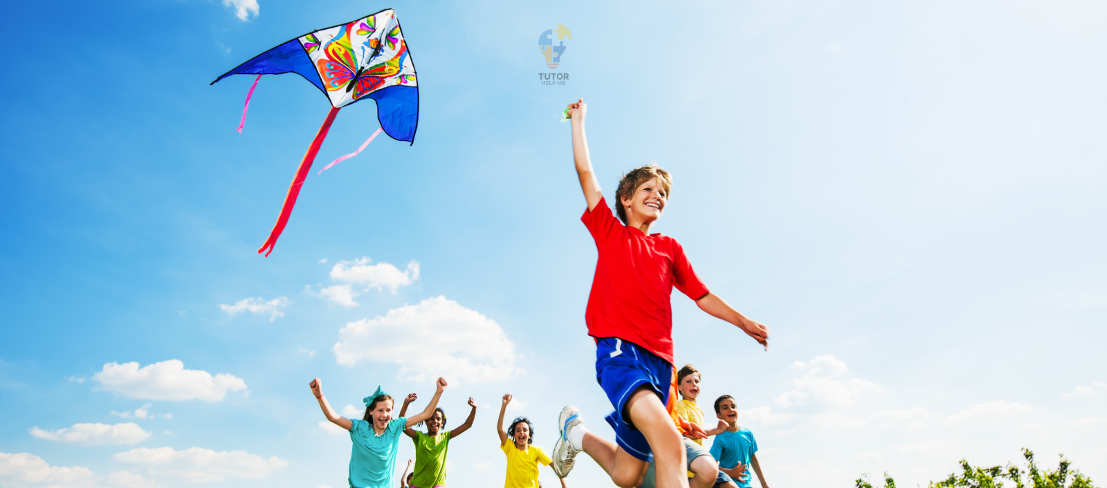Children joyfully fly a colorful kite under a bright blue sky, surrounded by fluffy white clouds.