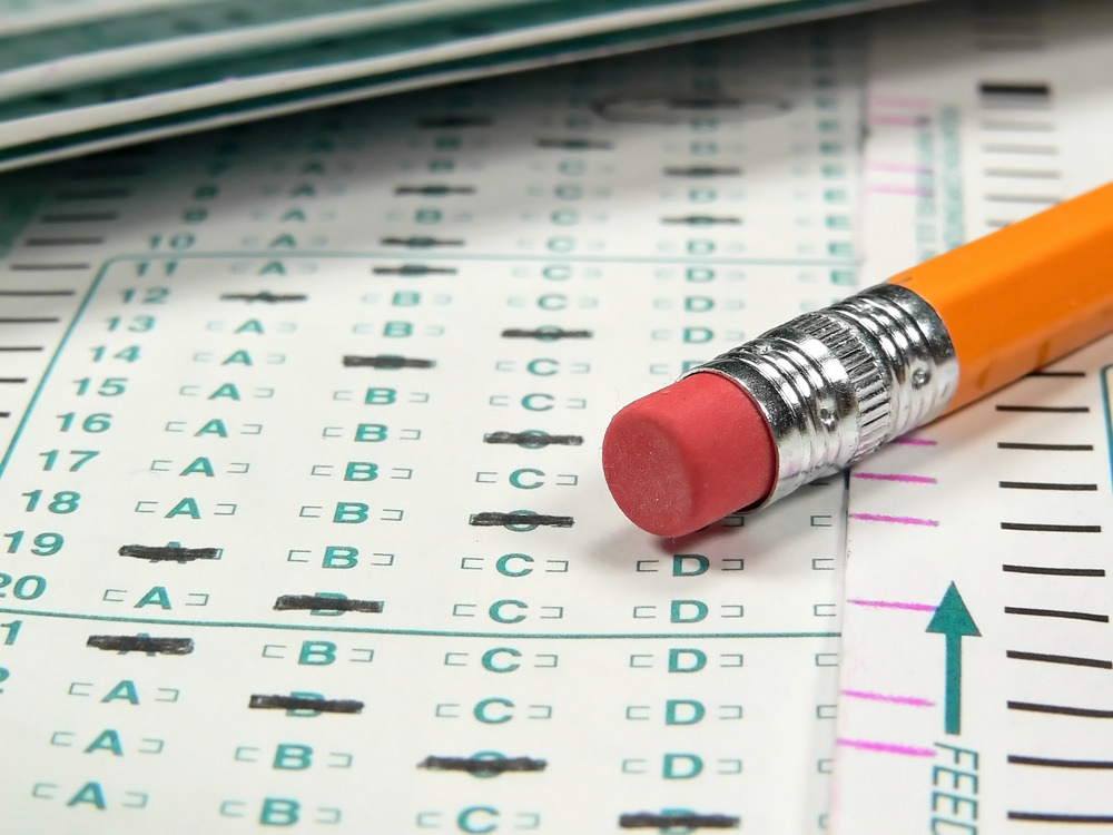 Close-up of an orange pencil with an eraser resting on printed answer sheets, marked with multiple-choice responses.