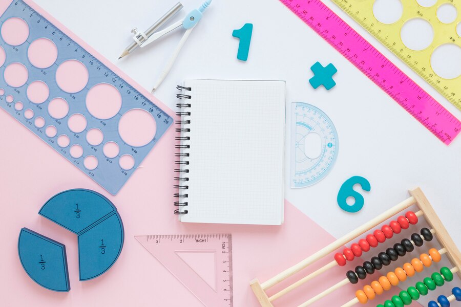 A collection of math supplies including a notebook, geometric tools, colored rulers, fraction shapes, and an abacus, arranged artistically.