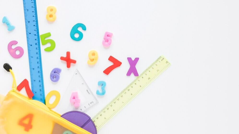 Colorful numbers and math symbols scattered around a yellow pencil case and rulers on a white surface, creating a playful study scene.