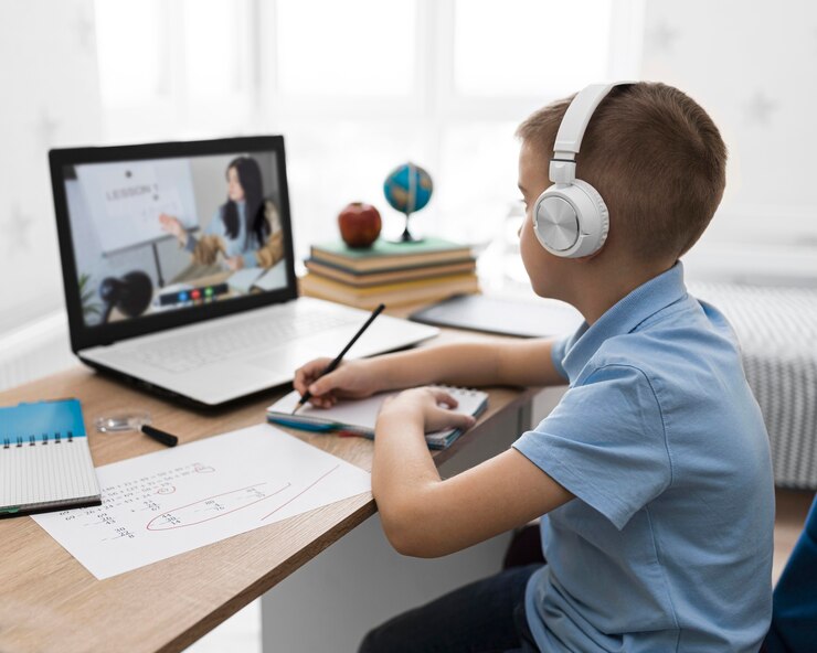 A child wearing headphones sits at a desk, engaged in online learning with a laptop, taking notes and solving problems.
