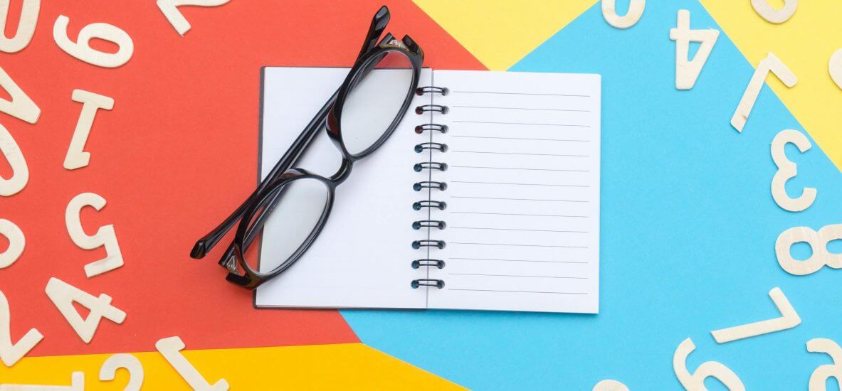 A pair of black glasses rests on a blank notebook, surrounded by colorful wooden numbers on a vibrant geometric background.
