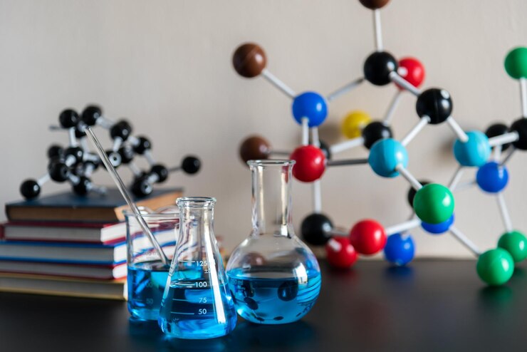 Laboratory scene with blue liquid in glass flasks, books stacked, and colorful molecular models in the background.