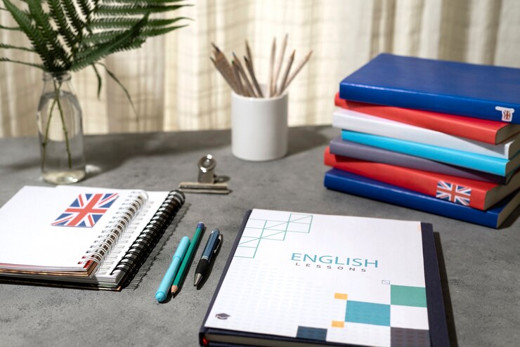 A study desk featuring English lesson materials, notebooks with a British flag, pens, and a plant in a small vase.