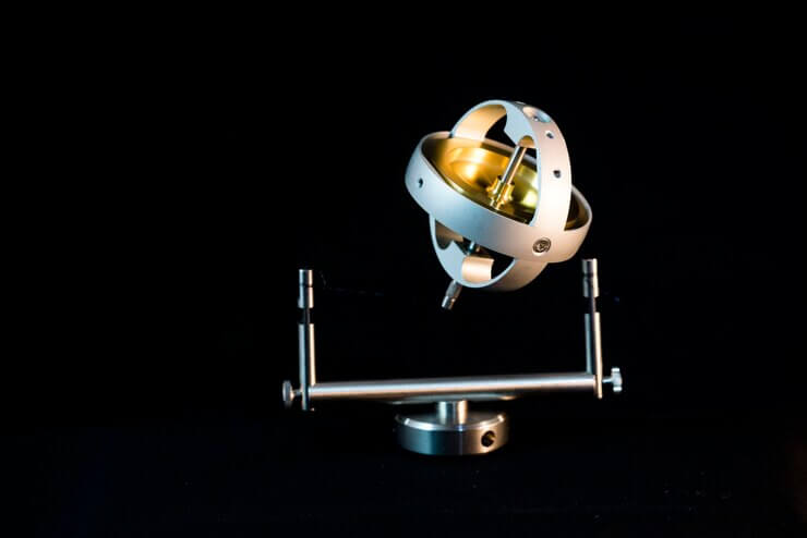 A metallic globe or orrery with silver and gold accents, mounted on a sleek stand against a black background.