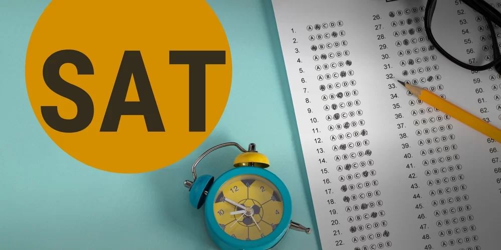 A turquoise alarm clock and a pencil lie beside an SAT answer sheet with "SAT" prominently featured on a bright orange circle.