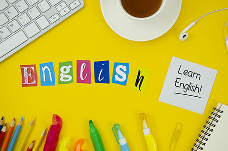 Colorful letters spelling "English," surrounded by stationery, a coffee cup, and a note saying "Learn English!" on a bright yellow background.