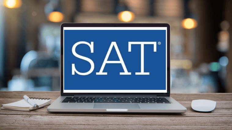A laptop on a wooden table displays the blue SAT logo, with a notepad and pen beside it in a softly blurred background.