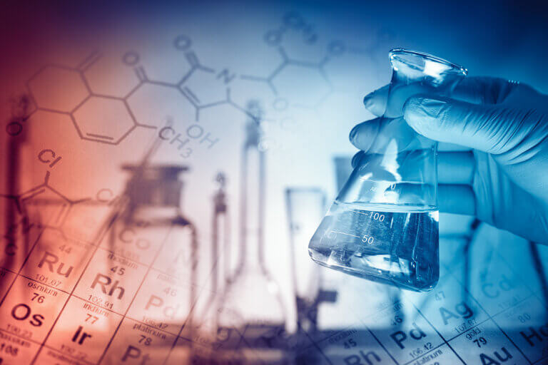 A gloved hand holds a glass flask with liquid, overlayed on a blurred periodic table, symbolizing scientific research and chemistry.