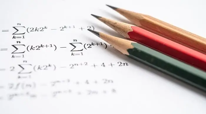 Close-up of mathematical equations on paper with three sharpened pencils in red, green, and natural wood at the forefront.