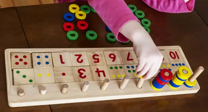 A child's hand arranging colorful wooden rings on a number-based educational toy, promoting counting and color recognition skills.
