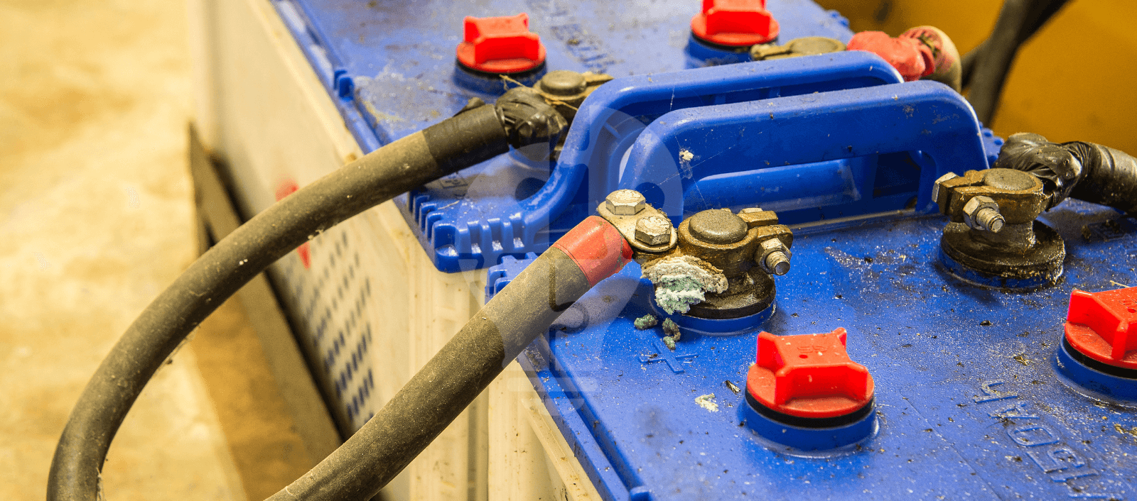 Close-up of a blue battery with red caps, featuring cables connected to terminals, showing some corrosion on the connections.