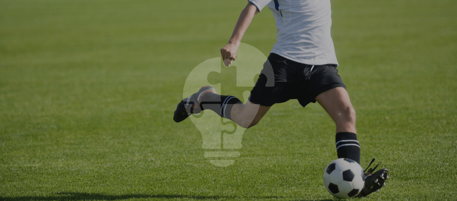 A player in a white jersey and black shorts kicking a soccer ball on a lush green field, showcasing athletic movement.