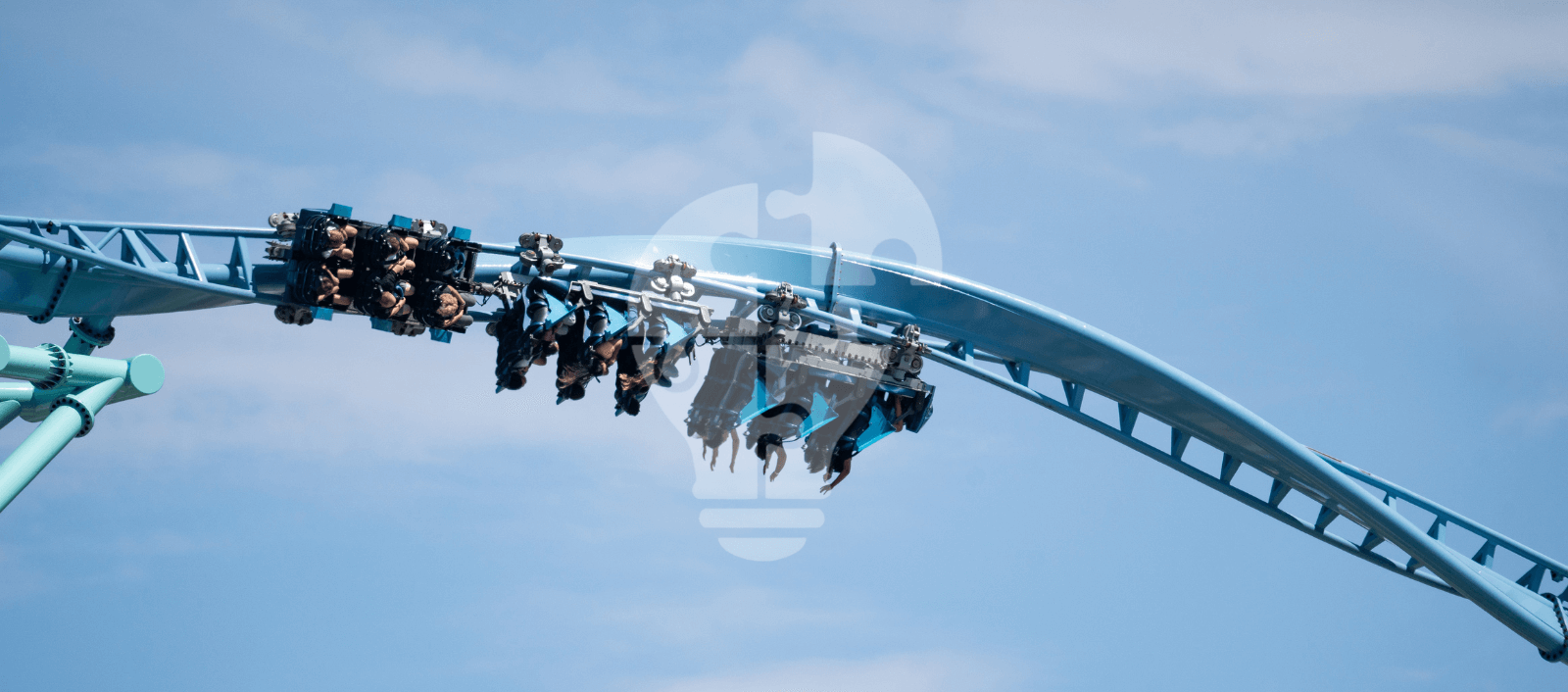 A roller coaster with riders suspended upside down on a bright blue track against a clear sky.