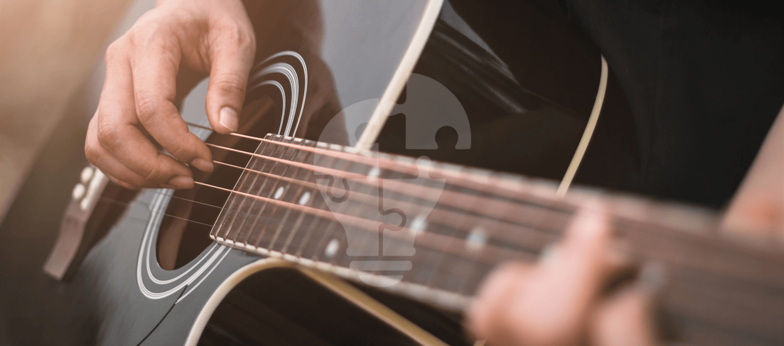 A close-up of a person’s hand playing an acoustic guitar, focusing on the strings and body of the instrument in warm, natural light.
