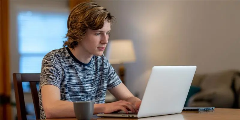 A person types on a laptop at a wooden table, with a coffee mug nearby and soft lighting in the background, creating a cozy atmosphere.